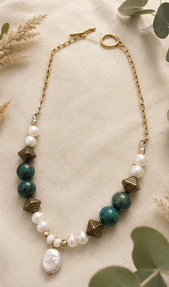 Collier POPPY en perles d'eau douce, pierres vertes et éléments dorés, présenté sur du sable clair avec des végétaux séchés